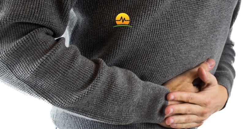 Man in gray sweater holds pressure against lower abdominal hernia may need hernia repair. MASJax logo at top center.