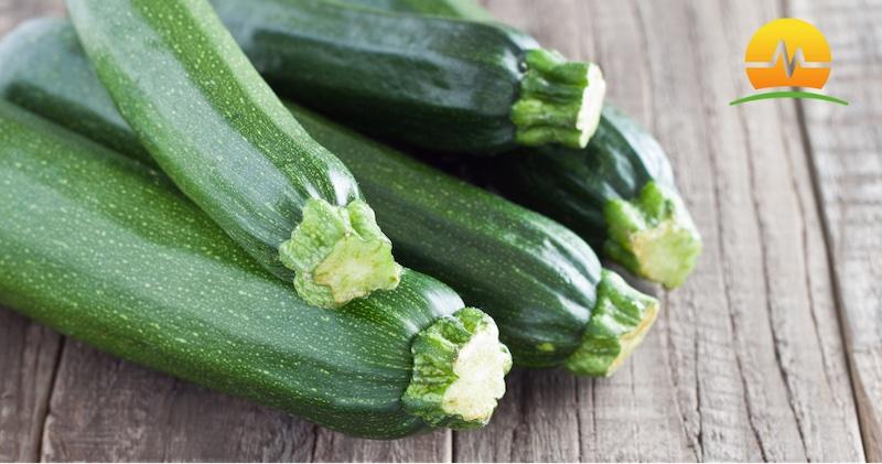 Five fresh zucchinis stacked on a wooden table to make chicken zucchini enchiladas. MASJax logo in top right corner.