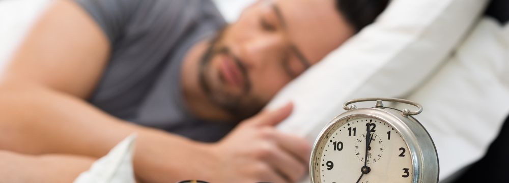 man sleeping behind alarm clock on night stand