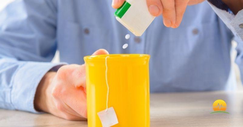 Man in blue dress shirt adds artificial sweetener tabs to mug hoping for a healthier option than sugar. MASJax logo at bottom right.