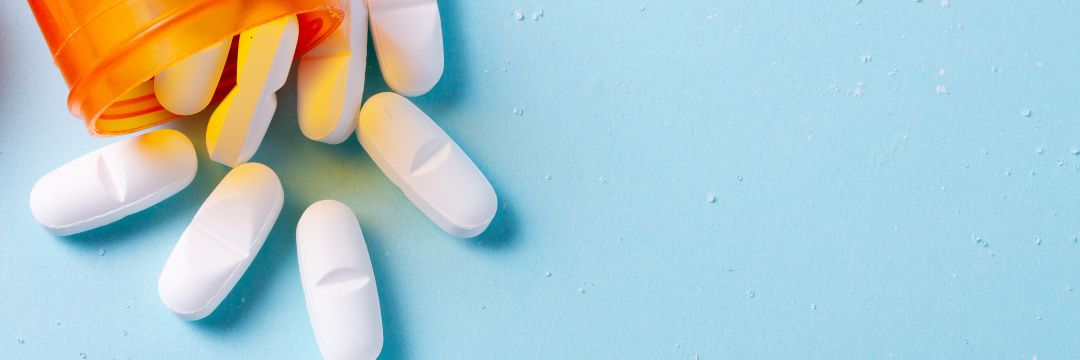 Orange bottle of white pills spilling onto blue background 