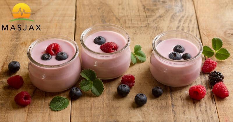 Three glass cups of yogurt topped with raspberries and berries on a wooden table. MasJax logo in top left corner.