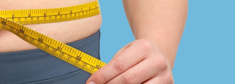Person measuring their waist size with yellow measuring tape