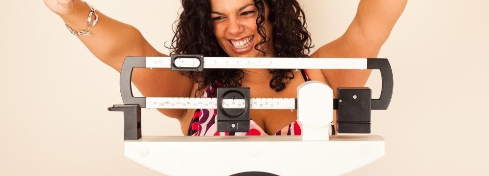 Woman smiling on a scale with arms raised looking at her weight