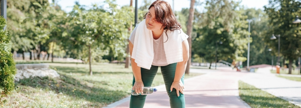 Out of breath woman hunched over with hands on knees after outdoor exercise