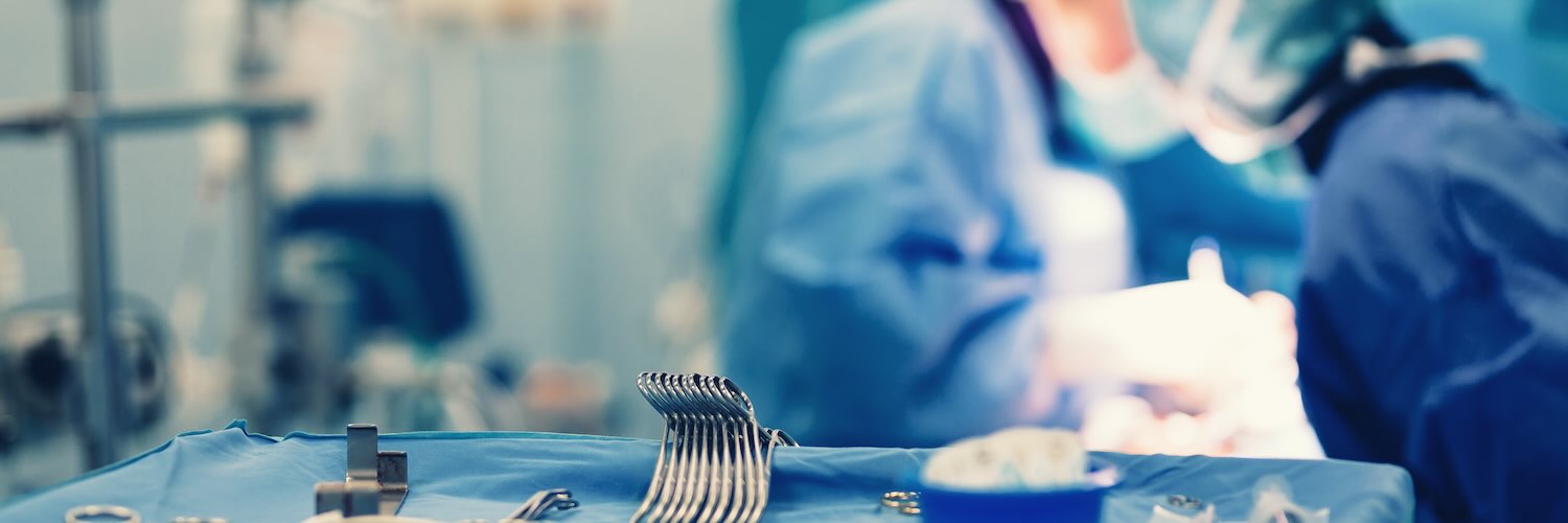 Operating room team works on surgery next to tray of surgical instruments 