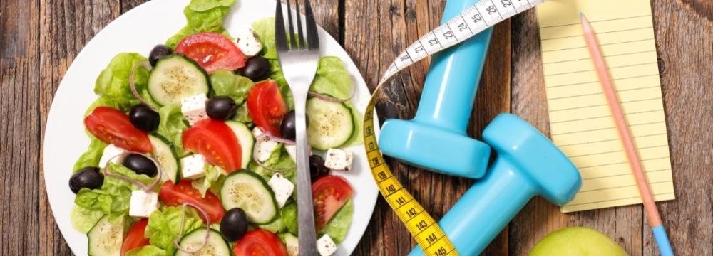 blue dumbbells, notepad with pencil and salad bowl with greens and veggies sitting on wooden table