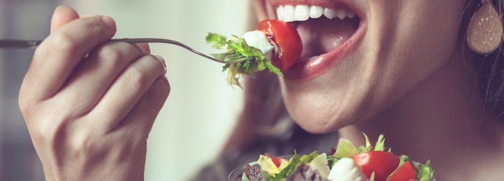 Woman eating salad with fork, mouth open