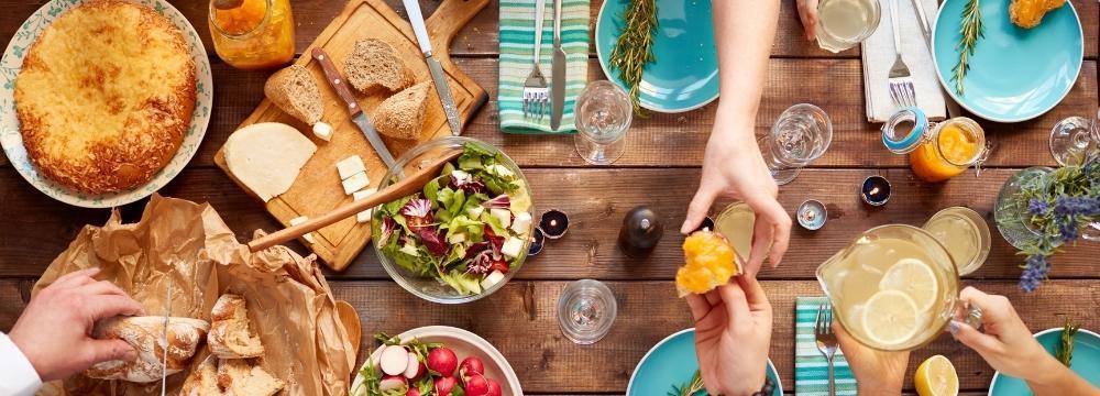 variety of dinner foods on a table, hands reaching for different food items